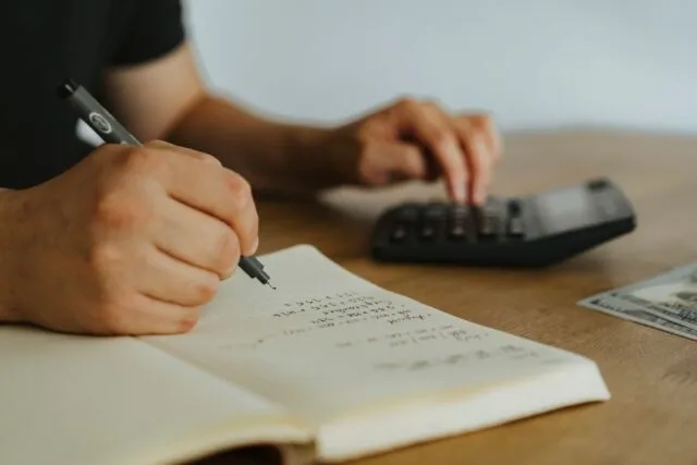 Birou cu calculator, caiet și cafea, unde cineva își socotește cheltuielile lunare